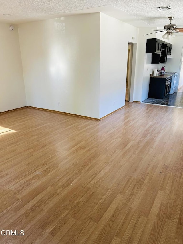 unfurnished living room with light wood-type flooring, ceiling fan, visible vents, and a textured ceiling