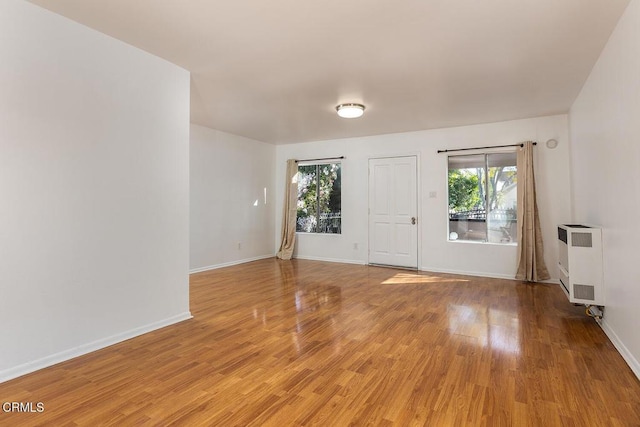 empty room with heating unit, light wood-style flooring, and baseboards