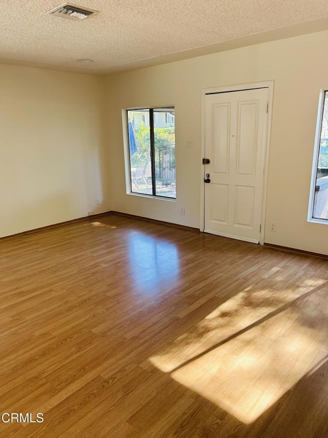 unfurnished room featuring baseboards, light wood-style flooring, visible vents, and a textured ceiling