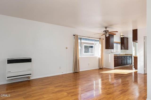 unfurnished living room with light wood-style floors, baseboards, ceiling fan, and heating unit