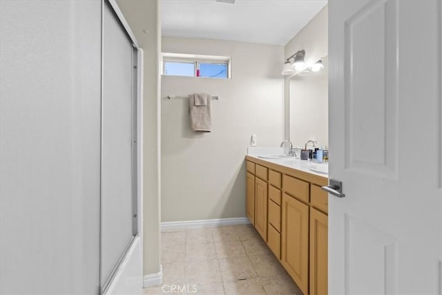 full bathroom featuring a sink, double vanity, baseboards, tile patterned floors, and a shower with shower door