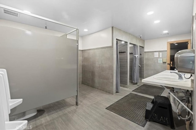 bathroom featuring a wainscoted wall, tile walls, visible vents, and a walk in shower