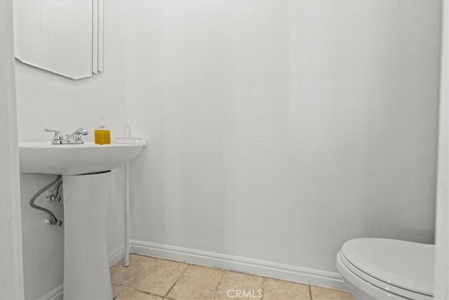 half bath featuring tile patterned floors, toilet, and baseboards