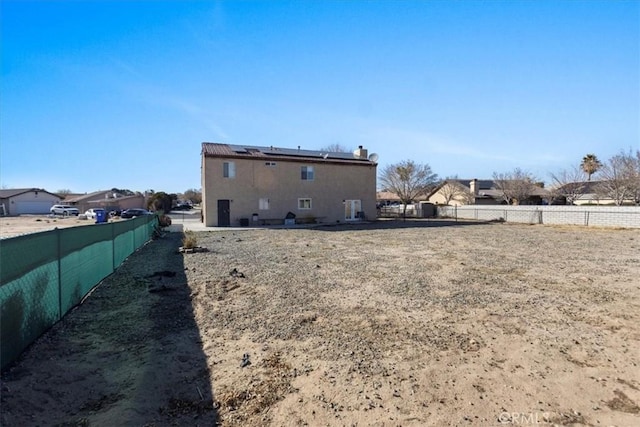 rear view of house with roof mounted solar panels and a fenced backyard