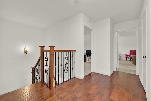 hall with baseboards, wood finished floors, and an upstairs landing