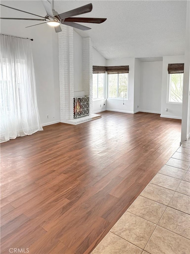 unfurnished living room with ceiling fan, wood finished floors, vaulted ceiling, a textured ceiling, and a fireplace