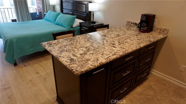 interior space with open floor plan, light tile patterned flooring, light stone countertops, a peninsula, and baseboards