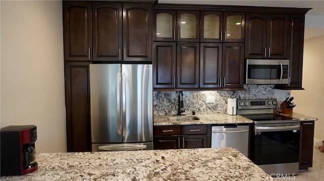 kitchen featuring light stone counters, dark brown cabinetry, stainless steel appliances, a sink, and tasteful backsplash