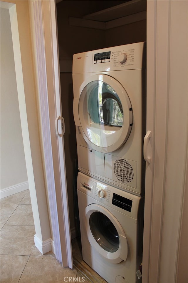 laundry area featuring stacked washer / drying machine, laundry area, light tile patterned flooring, and baseboards