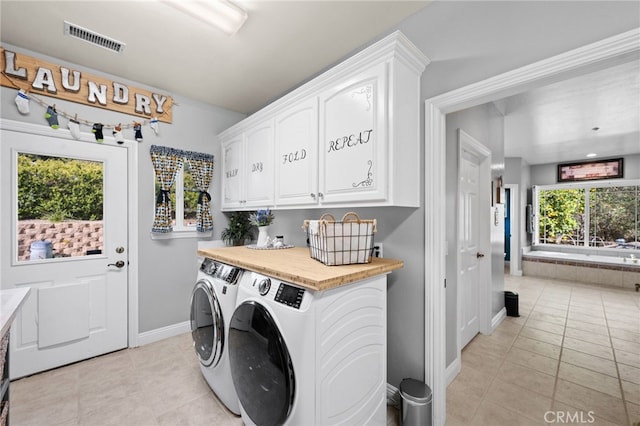 washroom featuring light tile patterned floors, visible vents, cabinet space, washer and dryer, and baseboards