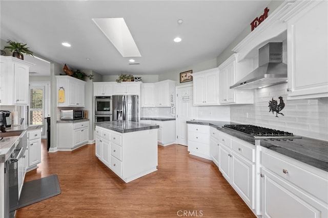 kitchen with white cabinets, a skylight, wall chimney exhaust hood, and stainless steel appliances