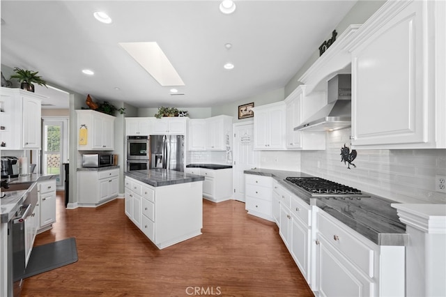 kitchen with a skylight, white cabinetry, appliances with stainless steel finishes, backsplash, and wall chimney exhaust hood