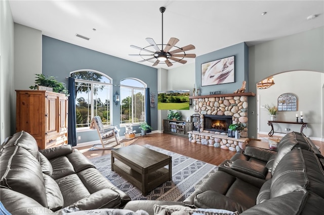 living area featuring baseboards, visible vents, arched walkways, wood finished floors, and a stone fireplace