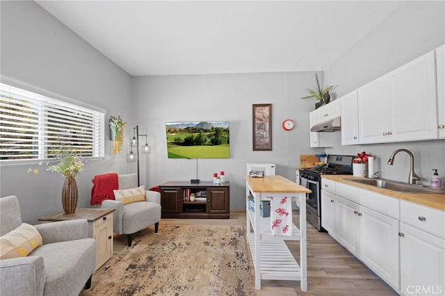 kitchen featuring a sink, white cabinets, open floor plan, light wood-type flooring, and gas stove