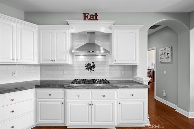 kitchen featuring dark wood-style flooring, white cabinetry, wall chimney exhaust hood, tasteful backsplash, and dark stone countertops