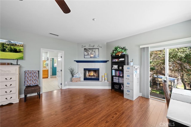 living area with a fireplace, visible vents, ceiling fan, wood finished floors, and baseboards