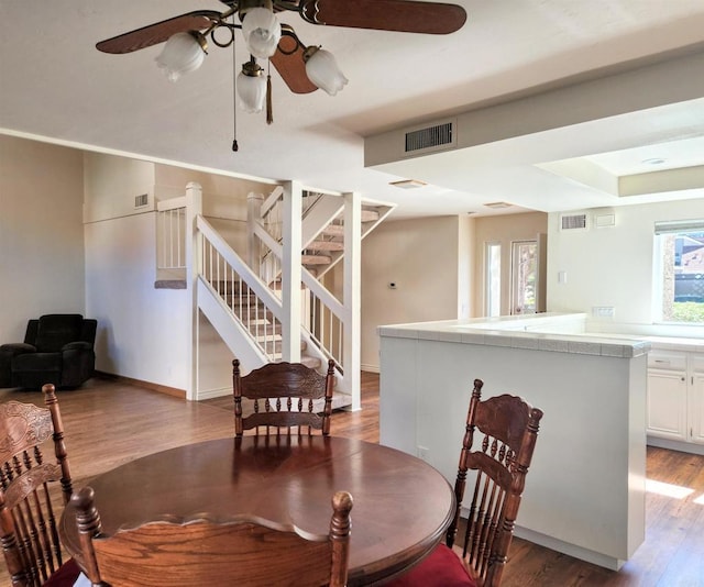 dining area with ceiling fan, stairway, light wood-type flooring, and visible vents