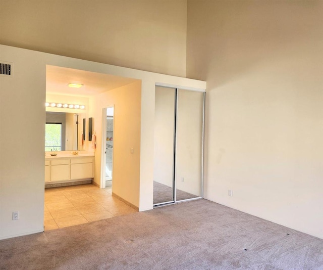 unfurnished bedroom featuring light carpet, light tile patterned floors, visible vents, ensuite bath, and a closet