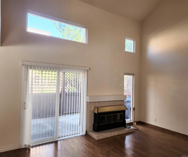 unfurnished living room featuring wood finished floors, a towering ceiling, and baseboards