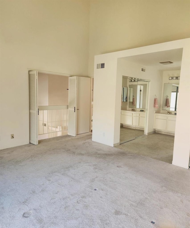 interior space featuring carpet, a high ceiling, visible vents, and ensuite bathroom