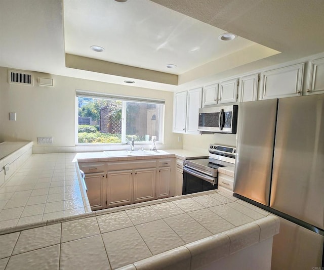 kitchen with tile counters, a raised ceiling, visible vents, appliances with stainless steel finishes, and a sink