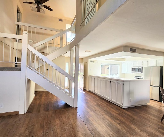 stairway with a towering ceiling, a ceiling fan, visible vents, and wood finished floors