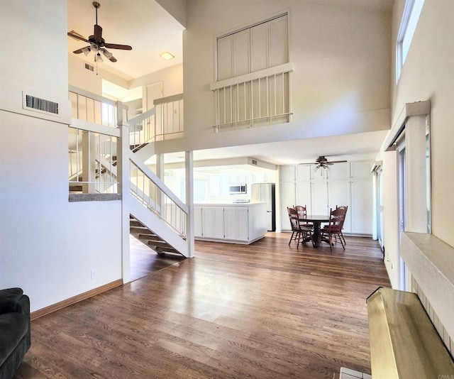 living area with dark wood-style floors, a high ceiling, visible vents, and a ceiling fan