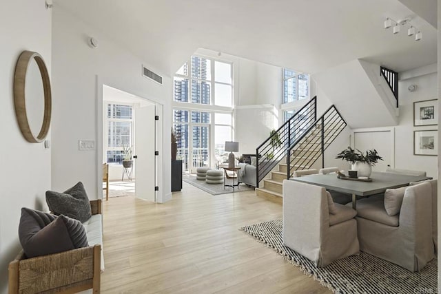 interior space featuring light wood finished floors, visible vents, stairway, a high ceiling, and expansive windows