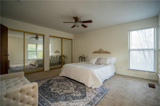 carpeted bedroom featuring a ceiling fan, visible vents, multiple closets, and baseboards