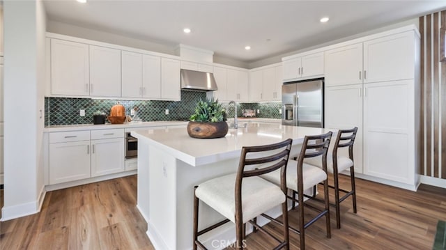 kitchen featuring under cabinet range hood, white cabinetry, appliances with stainless steel finishes, and wood finished floors