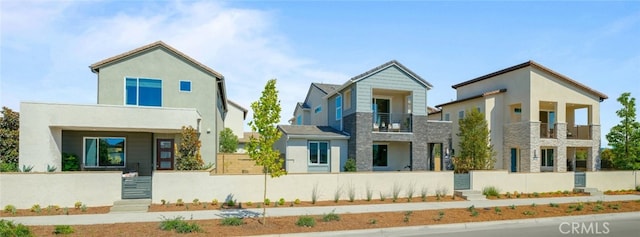 rear view of property featuring stone siding, a fenced front yard, a balcony, and stucco siding