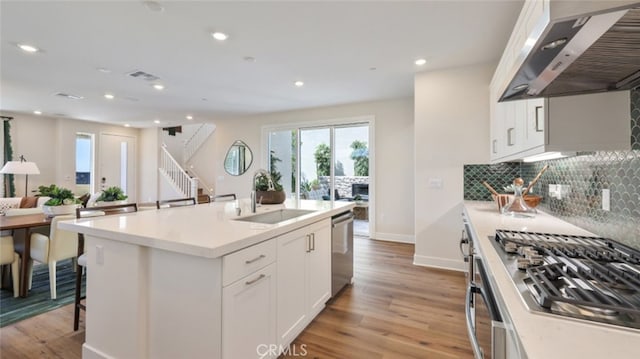 kitchen with under cabinet range hood, a sink, stainless steel dishwasher, light wood finished floors, and tasteful backsplash