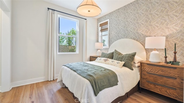 bedroom with wood finished floors, baseboards, and wallpapered walls