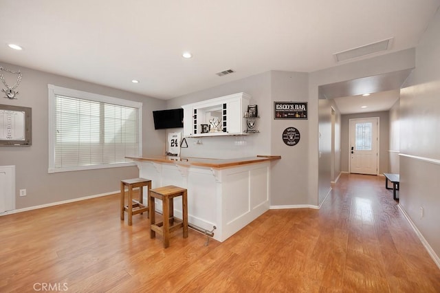 kitchen featuring light wood finished floors, open shelves, baseboards, visible vents, and a kitchen bar