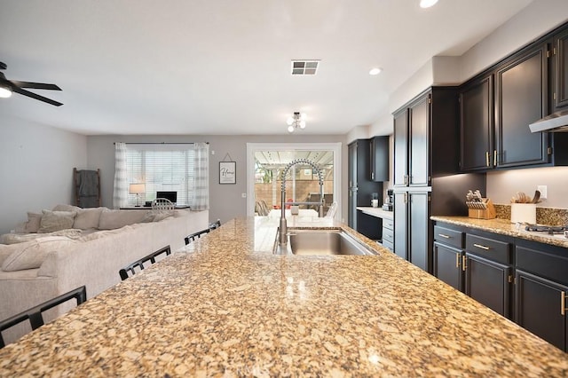 kitchen featuring open floor plan, a sink, visible vents, and light stone countertops