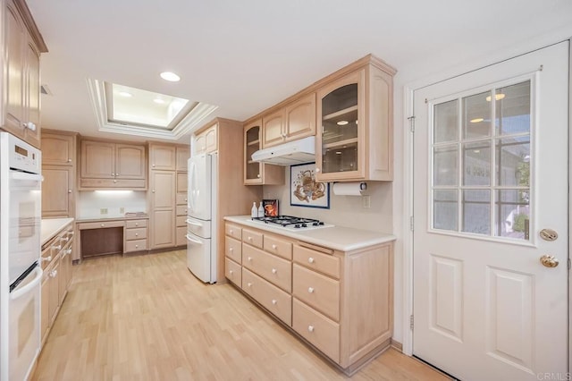 kitchen featuring light wood finished floors, a raised ceiling, light brown cabinets, white appliances, and under cabinet range hood