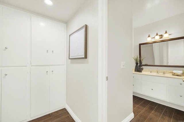 bathroom featuring wood finish floors, vanity, baseboards, and recessed lighting