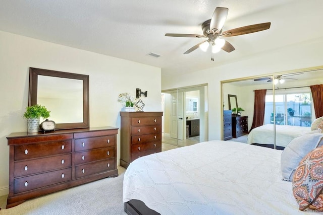 bedroom featuring visible vents, ceiling fan, light carpet, and two closets