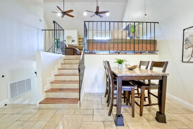 dining room featuring a high ceiling, visible vents, baseboards, stairs, and stone tile flooring