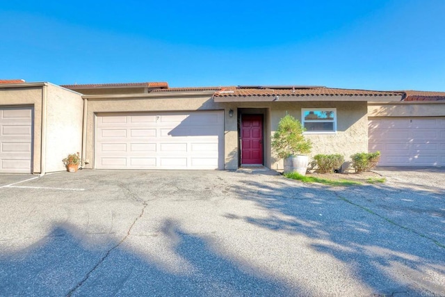 ranch-style house with a garage, solar panels, a tiled roof, and stucco siding