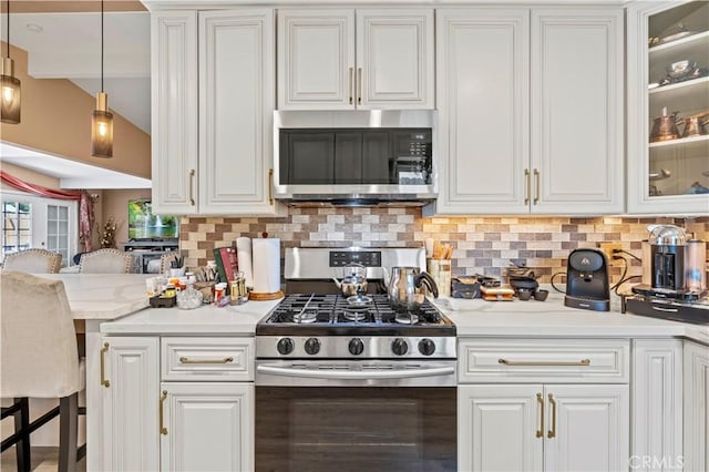 kitchen featuring stainless steel appliances, white cabinets, light countertops, tasteful backsplash, and glass insert cabinets