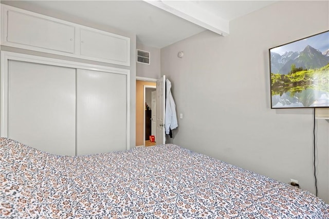 unfurnished bedroom featuring visible vents, a closet, and beam ceiling