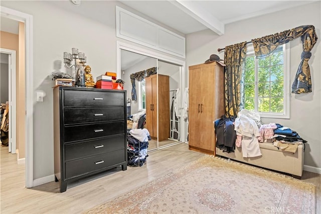 bedroom featuring light wood-style flooring, a closet, baseboards, and beamed ceiling