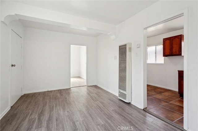 spare room featuring a heating unit, baseboards, and wood finished floors