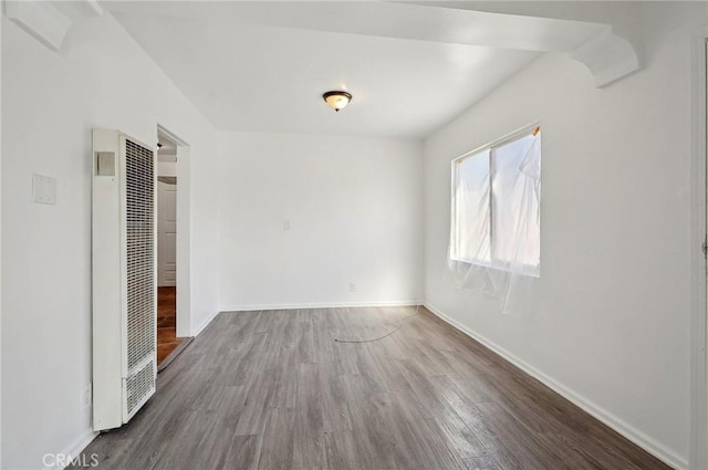 unfurnished bedroom featuring a heating unit, wood finished floors, and baseboards