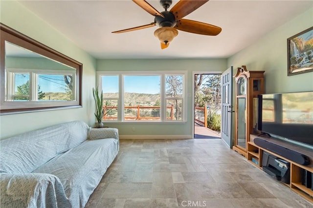 living area featuring stone finish floor, ceiling fan, and baseboards