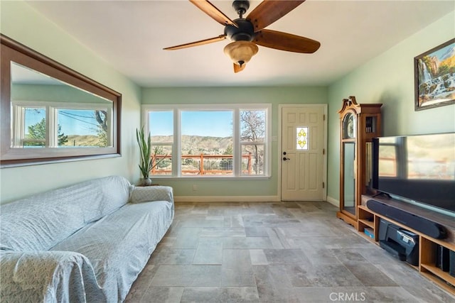 living area featuring ceiling fan, stone finish flooring, and baseboards