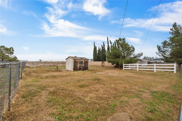 view of yard with a storage unit, a rural view, an outdoor structure, and fence