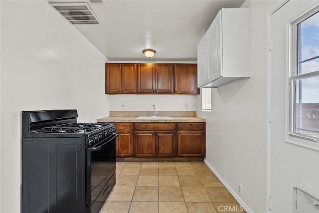 kitchen with tile countertops, light tile patterned floors, visible vents, black gas stove, and a sink