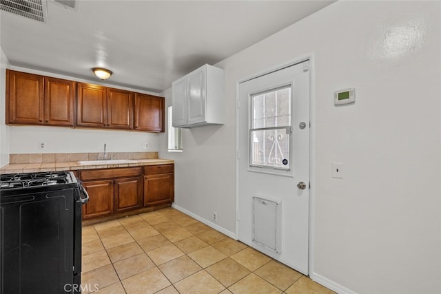 kitchen featuring visible vents, tile countertops, brown cabinets, black range with gas stovetop, and a sink